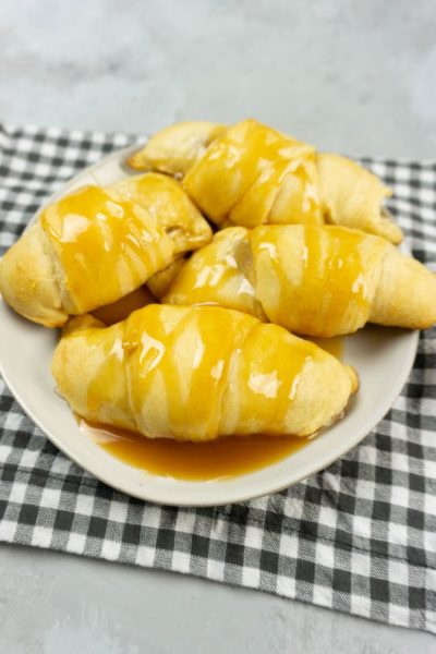 Apple Dumpling Croissants on a white plate with caramel drizzle with white and gray napkin on a concrete backdrop