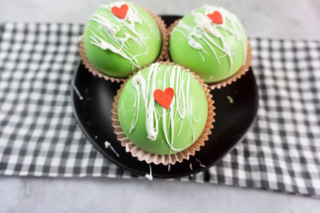Grinch Hot Chocolate Bombs on a black plate on a grey plaid napkin with a concrete backdrop