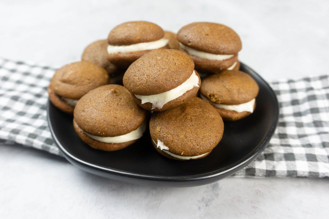 Pumpkin Whoopie Pies on a black plate with gray and white plaid napkin on a concrete backdrop