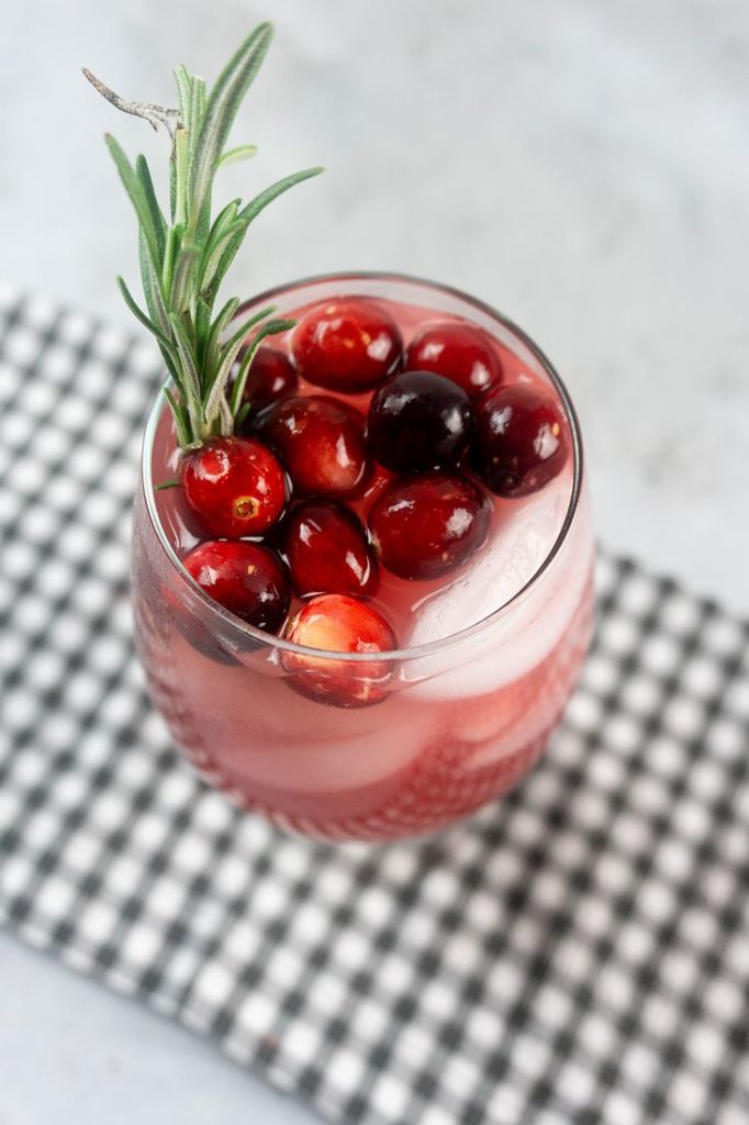 Rudolph Spritzer with cranberries and fresh rosemary in a glass on a gray plaid napkin and concrete backdrop