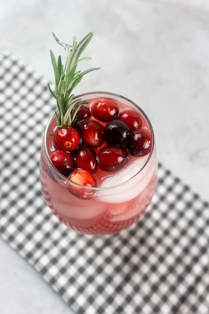 Rudolph Spritzer with cranberries and fresh rosemary in a glass on a gray plaid napkin and concrete backdrop