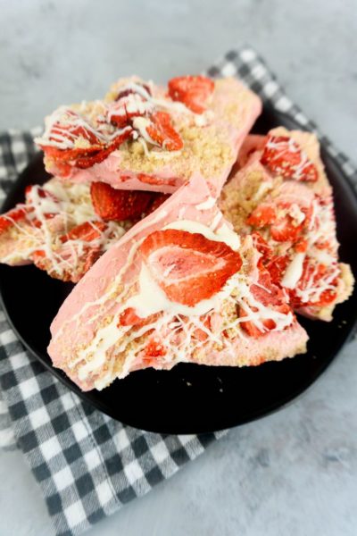 Strawberry Shortcake Bark on a black plate with grey and white plaid napkin on a concrete backdrop